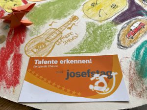 Kunstaktion bei der Auftaktveranstaltung des Josefstags. Vorne auf einer Collage liegt die Josefstags-Postkarte mit dem Motto.