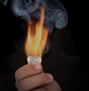 Eine Hand hält eine Euro-Münze. Diese geht nach oben hin in Flammen auf. Es bilden sich Rauchwolken. Das soll die hohe Inflation im Euro-Raum symbolisieren.
