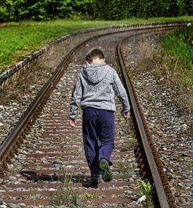 Zwischen ein paar Bahngleisen geht ein Junge alleine und mit gesenktem Kopf. Das Bild vermittelt den Eindruck von Einsamkeit und Traurigkeit.