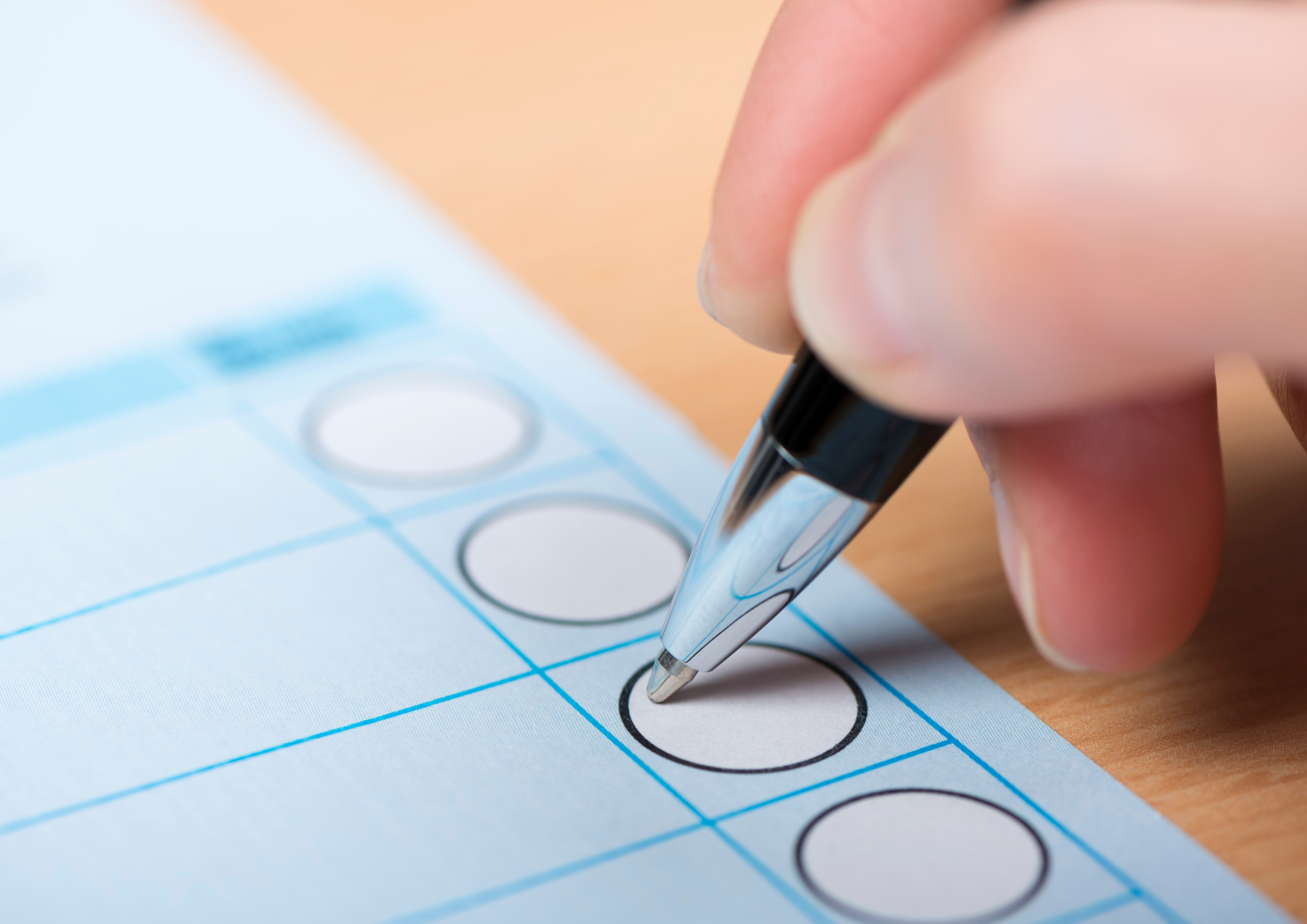 Der Bildausschnitt zeigt eine Hand, die mit einem Kugelschreiber ein Kreuz auf einem blauen Wahlzettel machen möchte.