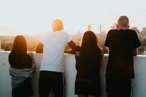 Man sieht vier junge Menschen von hinten, die an einer Mauer lehnen und über diese in die Stadt blicken.