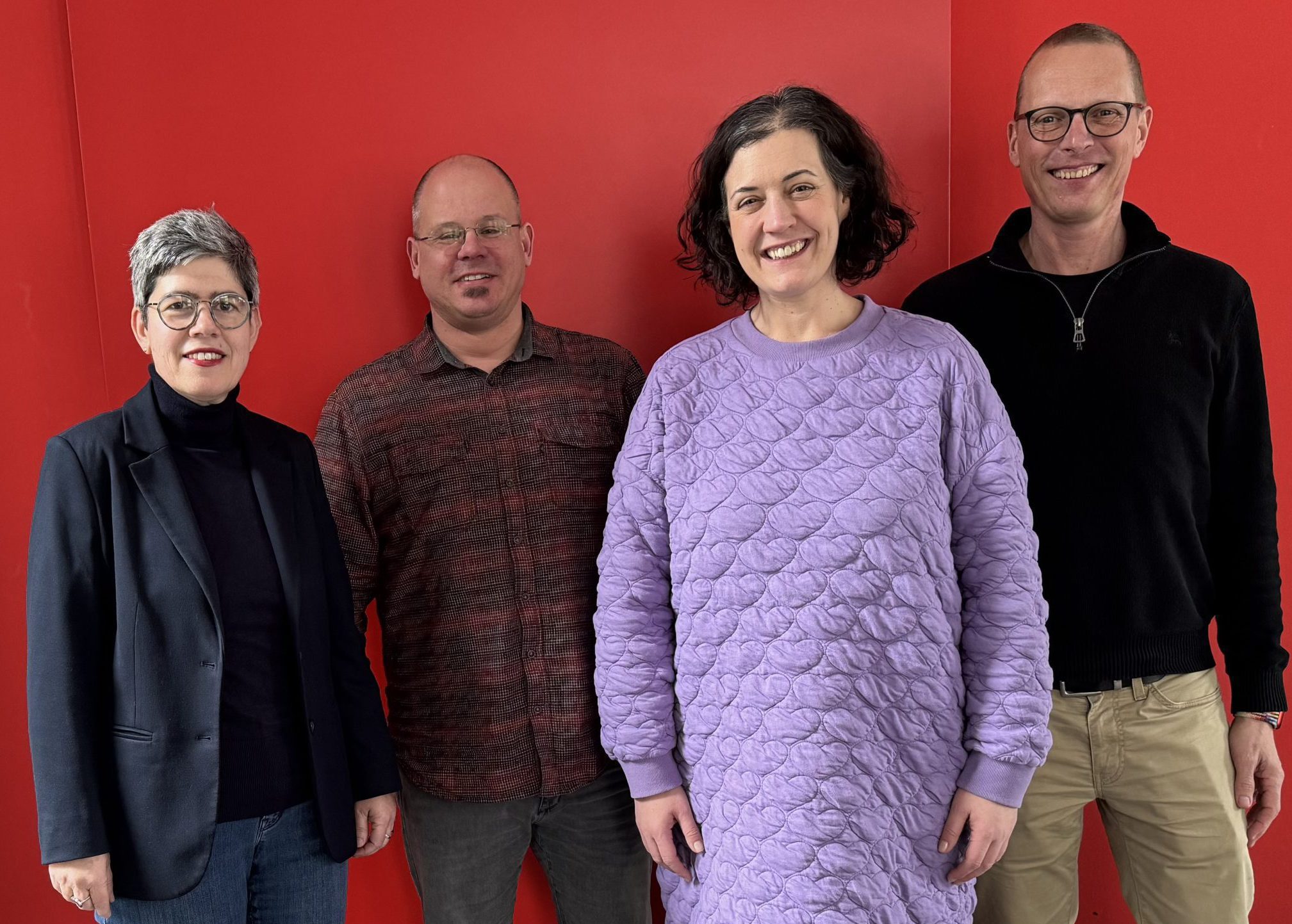 Das Bild zeigt den Vorstand der BAG KJS, wie er vor einem roten Hintergrund steht. Von links nach rechts sind dies Monika Kleinefeen, Stefan Ewers, Lena Bloemacher und Michael Kroll.