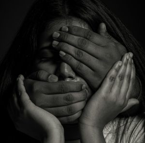 Das Schwarz-Weiß-Bild zeigt den Kopf einer dunkelhäutige Frau, die versucht mit ihren Händen ihren Kopf zu stützen, während ihr der Mund und die Augen von einer anderen Hand zugehalten werden.