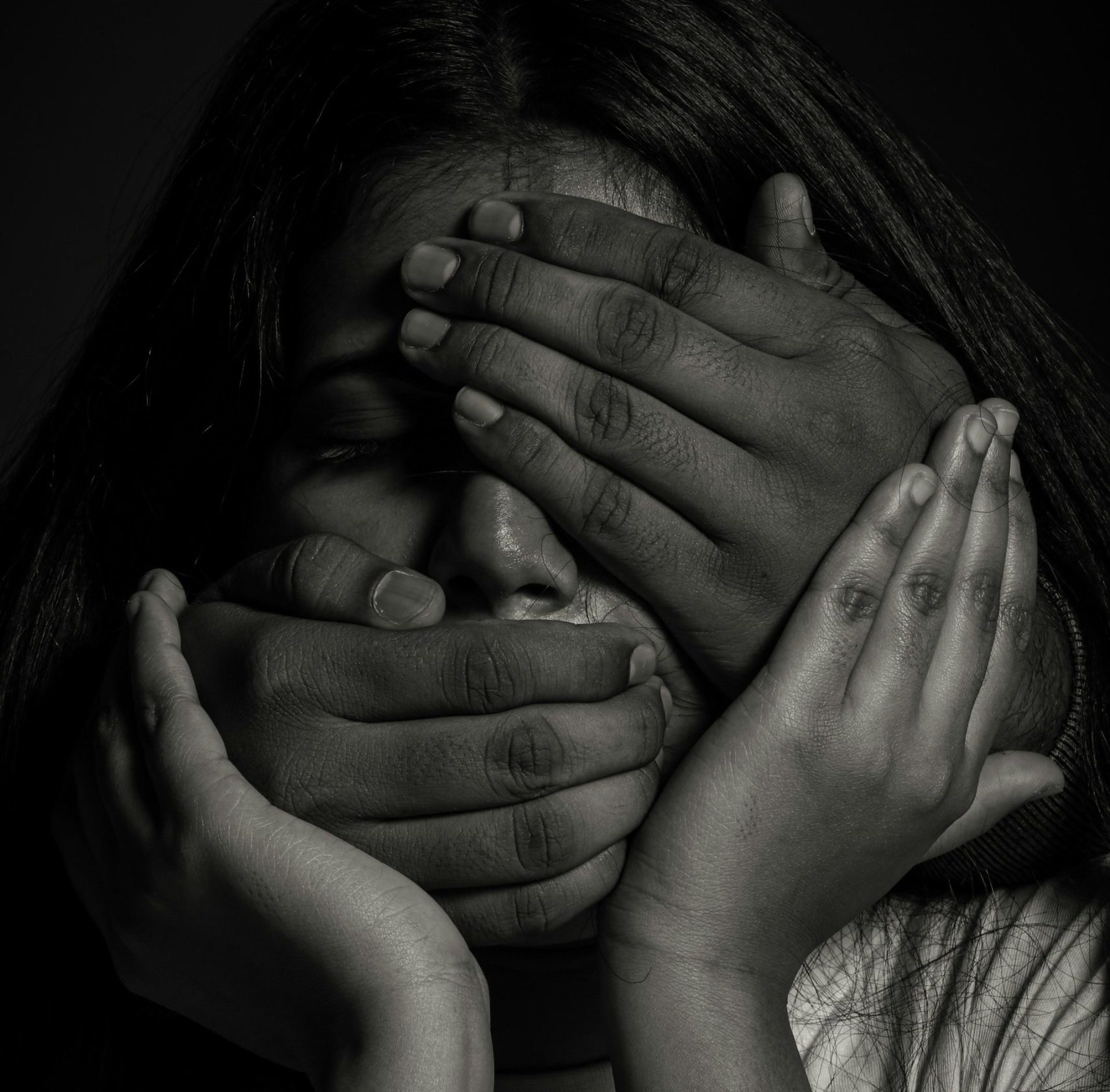 Das Schwarz-Weiß-Bild zeigt den Kopf einer dunkelhäutige Frau, die versucht mit ihren Händen ihren Kopf zu stützen, während ihr der Mund und die Augen von einer anderen Hand zugehalten werden.