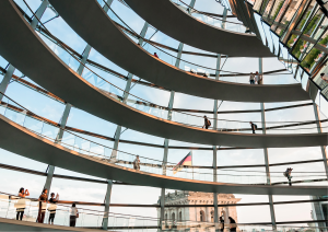 Zu sehen ist das Innere der Kuppel des deutschen Bundestages: Mehrere Gänge übereinander vor einer Glasfront.