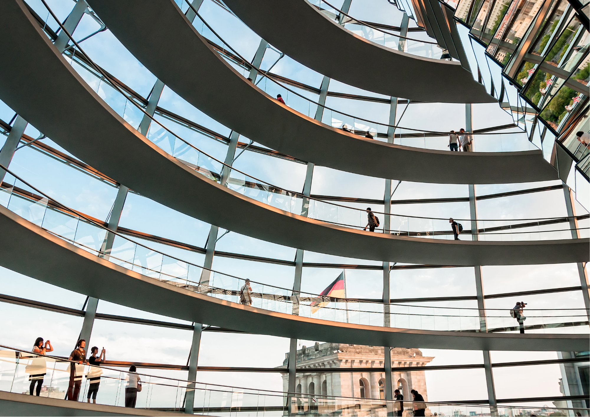 Zu sehen ist das Innere der Kuppel des deutschen Bundestages: Mehrere Gänge übereinander vor einer Glasfront.