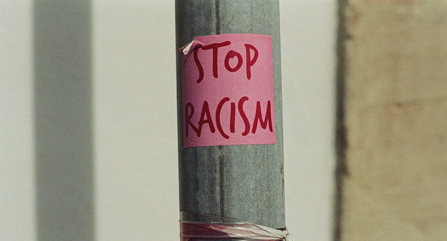 Ein Metallpfahl auf dem ein rosa Post-It klebt, auf dem "Stop Racism" in Großbuchstaben geschrieben steht.