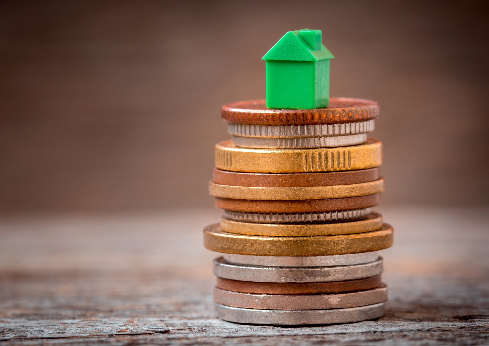 Ein kleines grünes Häuschen steht auf einem Haufen Münzen.