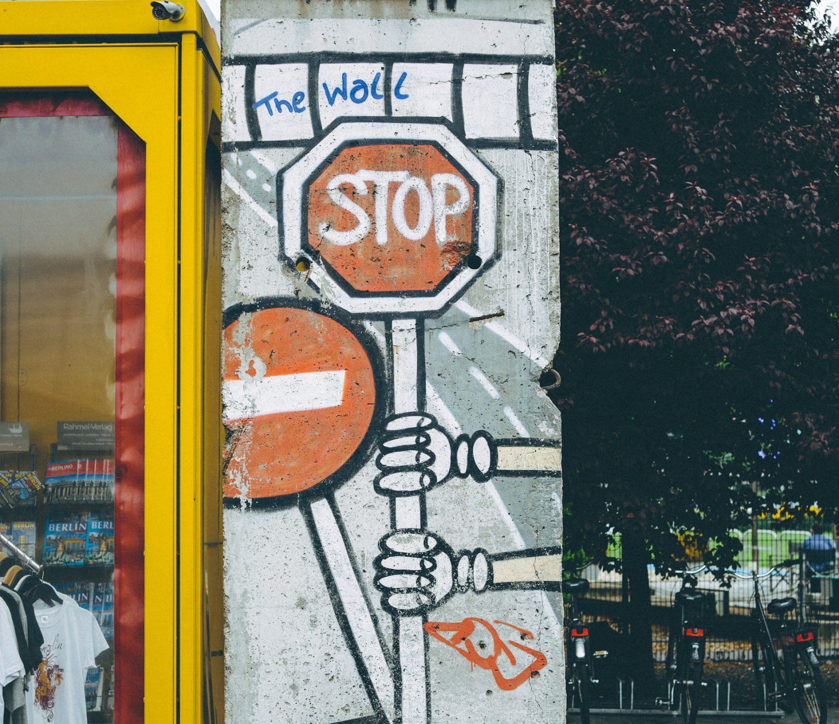 Ein Stoppschild-Graffiti, an dem sich zwei Hände festhalten, auf einer Mauer neben einer Telefonzelle.