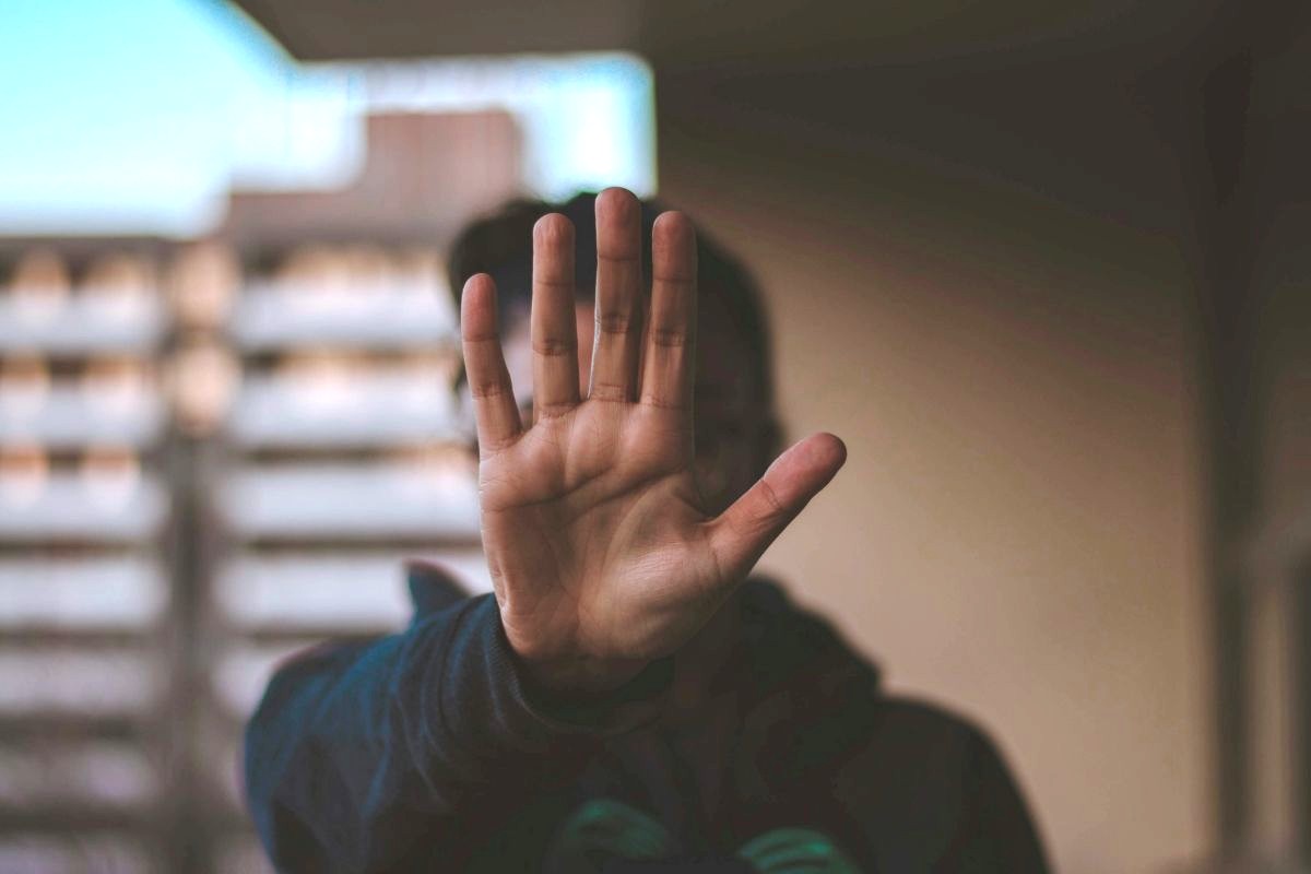 Mensch hält die Hand abwehrend vor das Gesicht, Hochhäuser im Hintergrund.